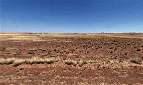 Aerial view of Arizona Navajo County 1.25-acre Rancho Lot 48 in Arizona, showing open land with desert landscape and distant mountains.