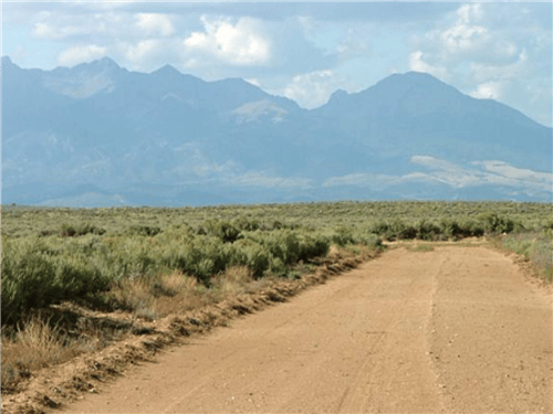 A scenic view of a 6.9-acre lot in San Luis Estates South, Colorado, with open land and mountains in the background.